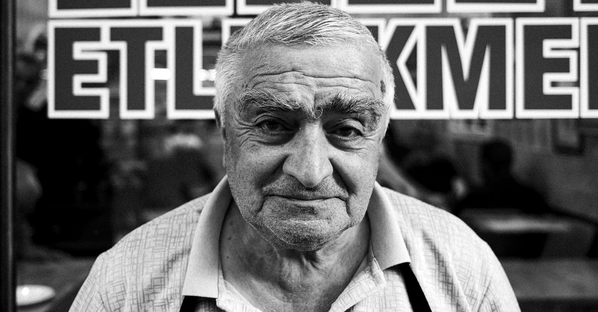 Black and white portrait of an elderly man in front of a sign in Akşehir, Konya, Türkiye.